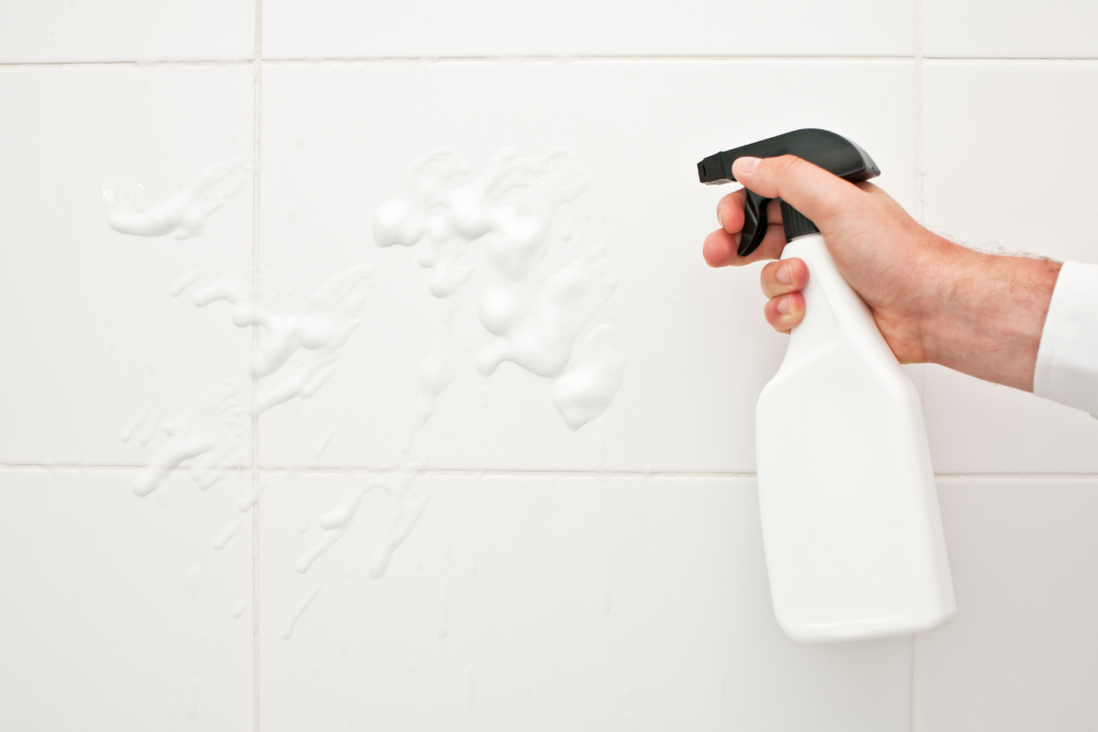 someone holding a bathroom cleaner in a spray bottle to clean the shower ceramic tiles without scrubbing