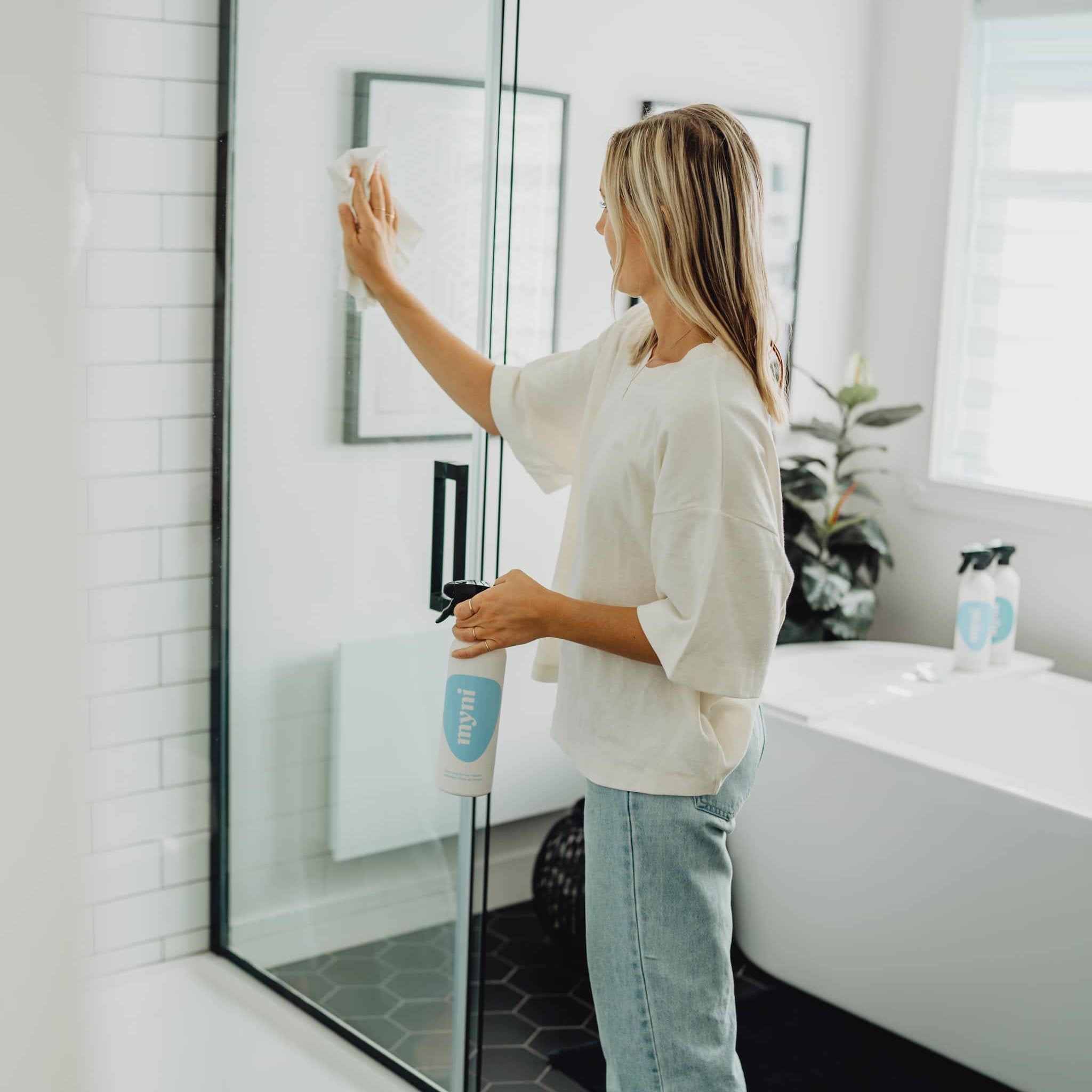 woman cleaning her shower glass door with myni's glass & mirror cleaner