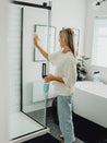 woman cleaning her shower glass door with myni's glass & mirror cleaner